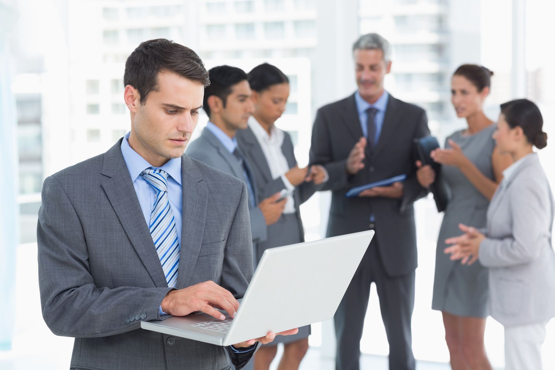 Businessman in a suit reviewing email on a laptop with colleagues