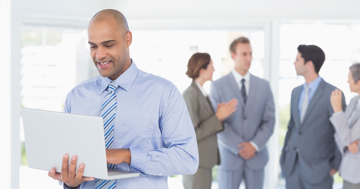 The Cybersecurity Executive Summary Every CEO and IT Manager Should See 7 Business manager working on a laptop with colleagues behind him, illustrating the CDK Global ransomware attack